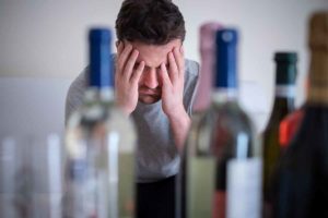 man sitting in front of bottles struggling with alcohol abuse triggers