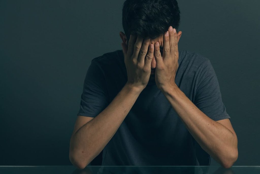 a man with his face in his hands thinking about the signs of meth addiction