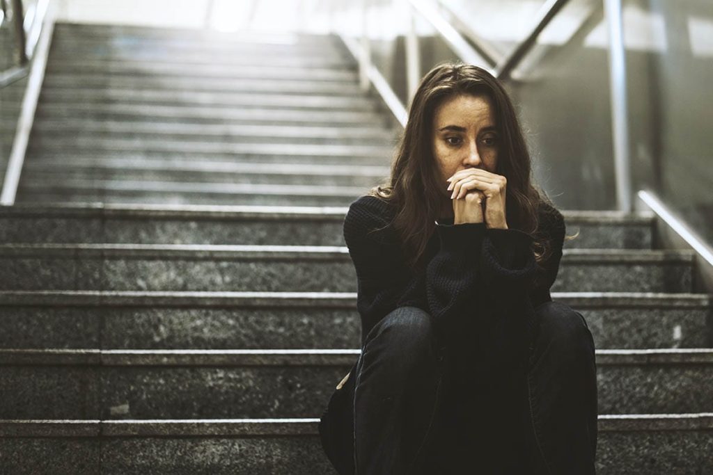 a woman sitting on a staircase with her hands to her chin thinking about the signs of an opiate overdose
