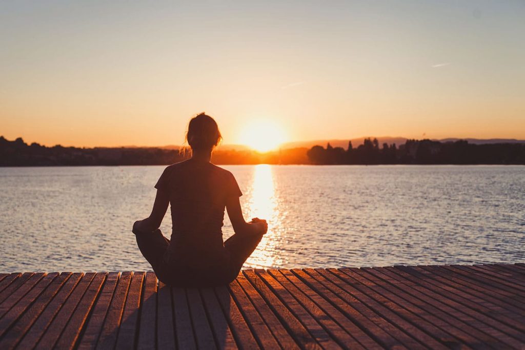 a woman sits on a dock and wonders about reasons to choose holistic treatment